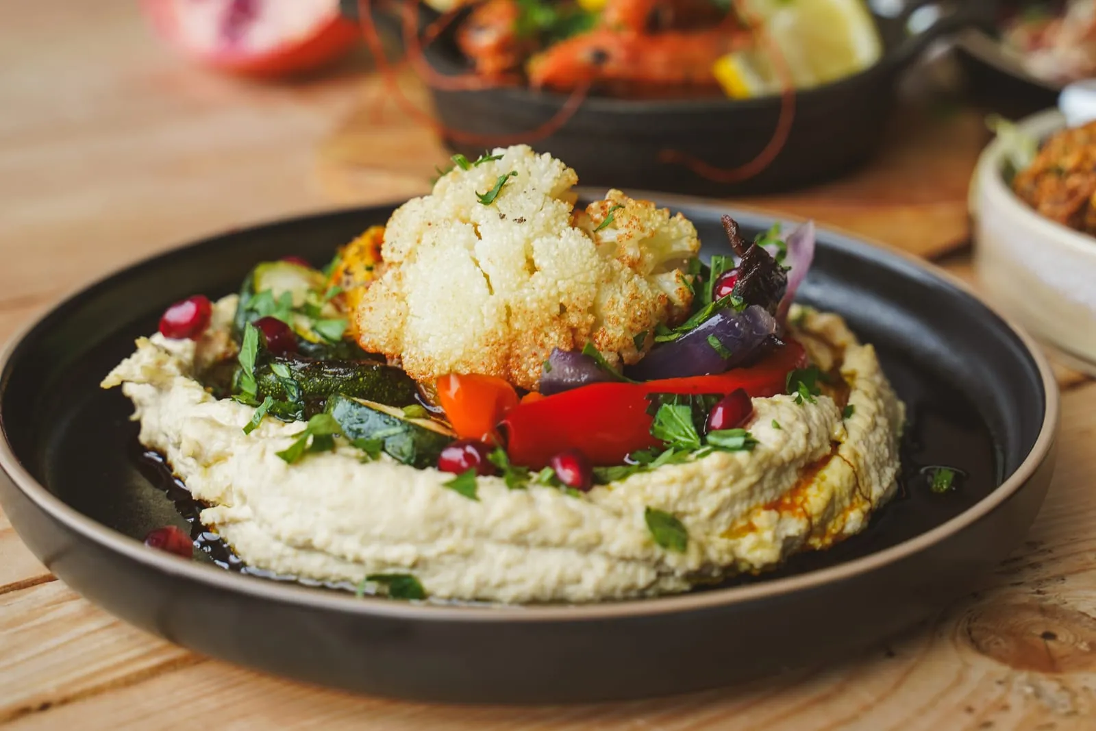 A bowl of ZHUG hummus topped with roasted cauliflower, peppers and pomegranate seeds