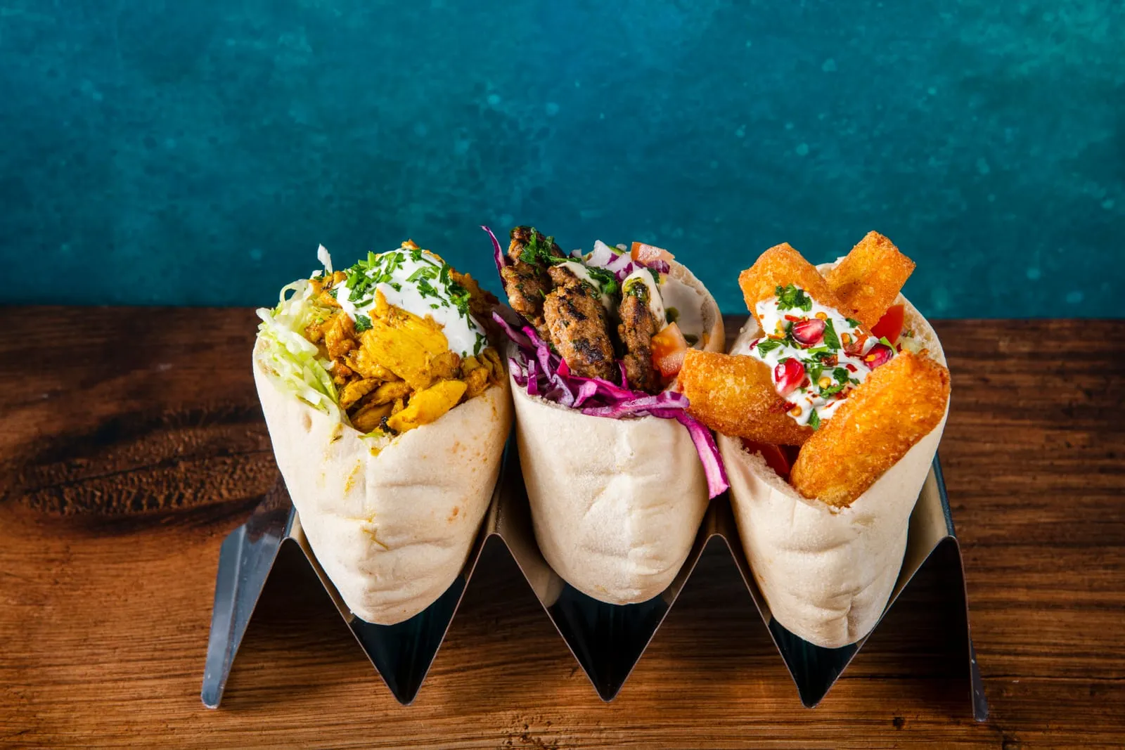 Three ZHUG pitas in a stand, filled with chicken, halloumi fries and salad